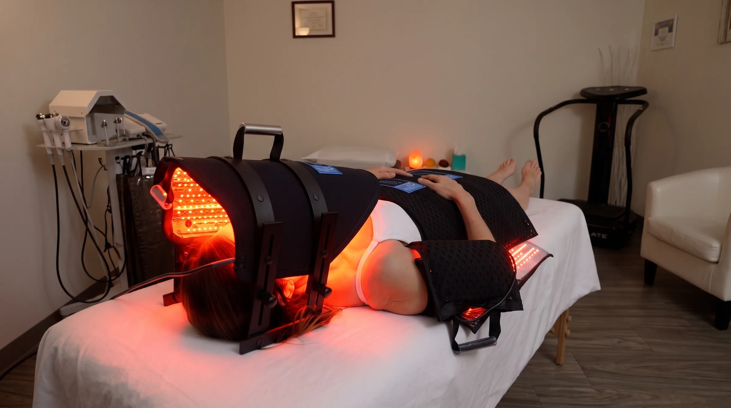 A client lying under the clinic's full-body red light system, wrapped in glowing LED pads